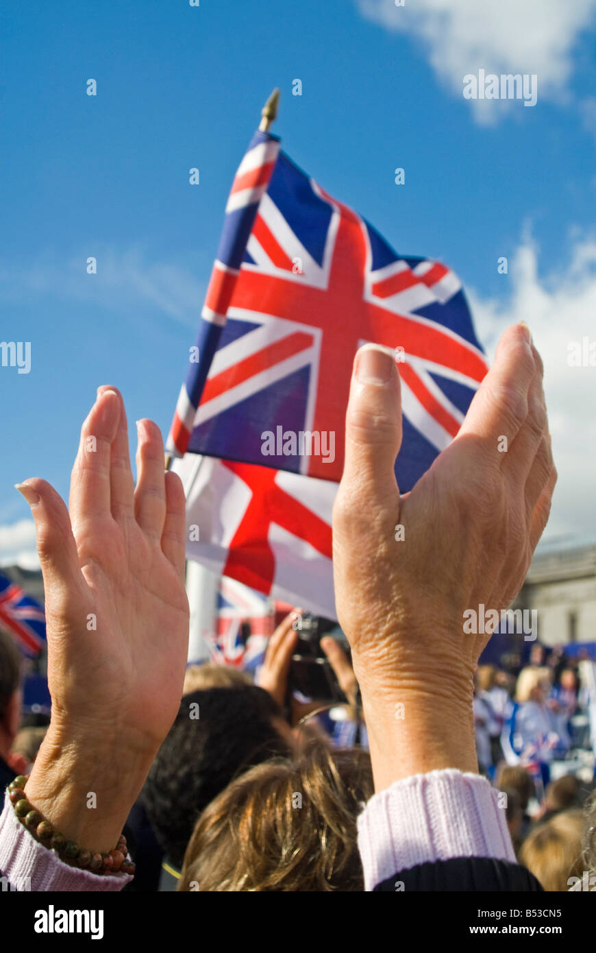 Vertical close up of crowds clapping and waving Union Jack and St George Cross flags at a celebration in London. Stock Photo