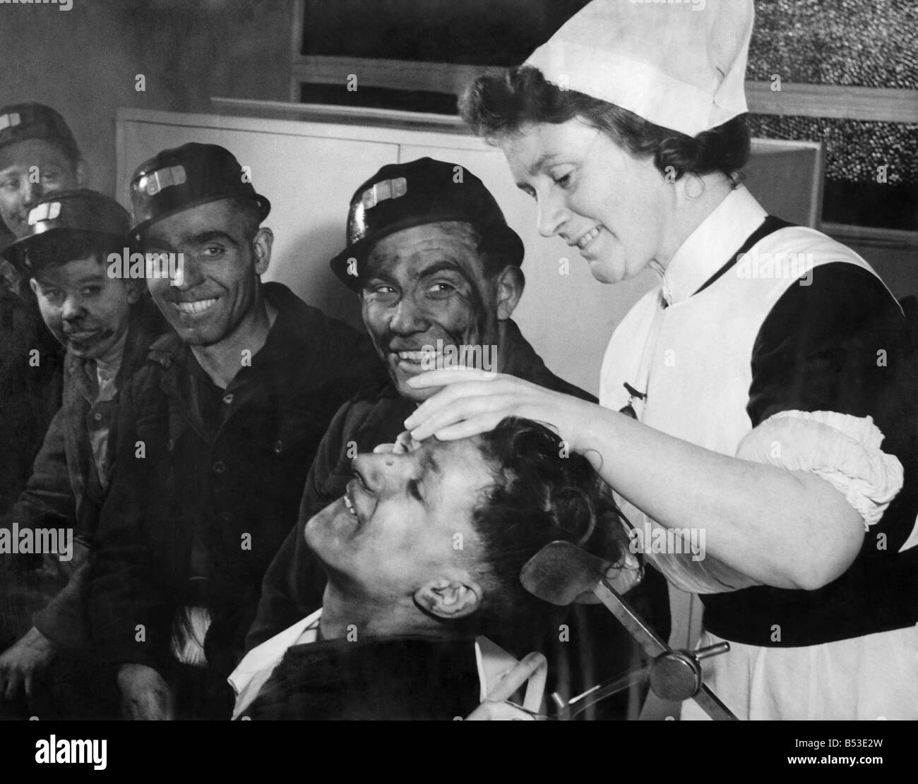 Cyril Annisworth, a 16 years old screen worker bites his lip as sister Ada swabs out his eye which had been covered with coal dust. His mates who are waiting their turn for attention from the sister make joking remarks. January 1948. P018136 Stock Photo