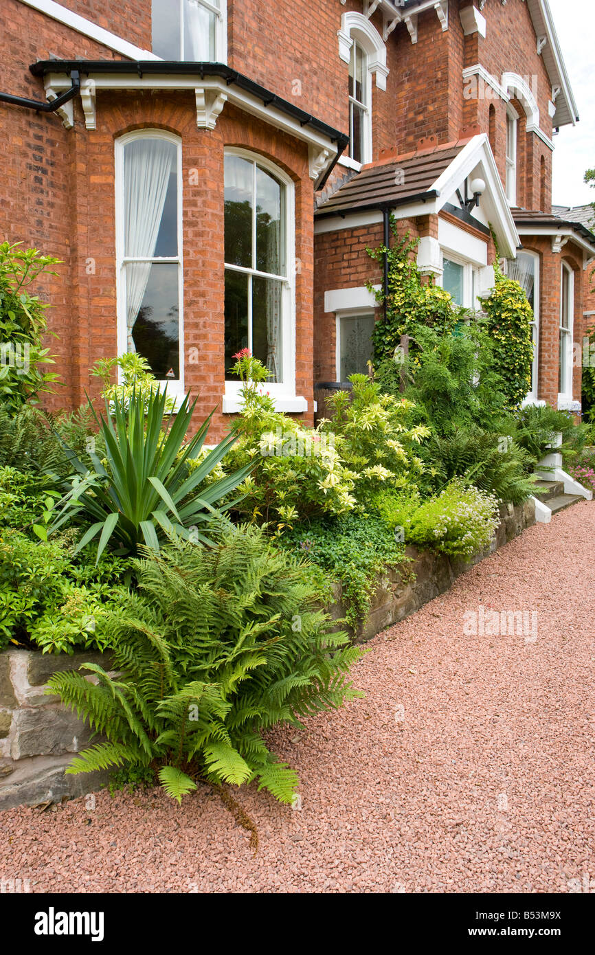 front garden of a large detached house with red gravel driveway and holly bushes Stock Photo