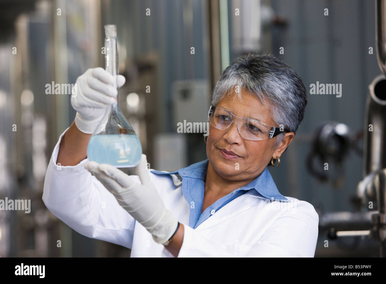 African scientist examining beaker of liquid in factory Stock Photo
