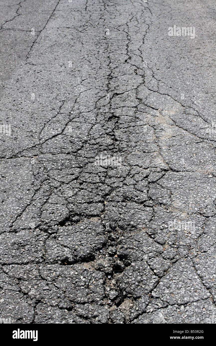 Cracked and crumbling asphalt road surface. Stock Photo