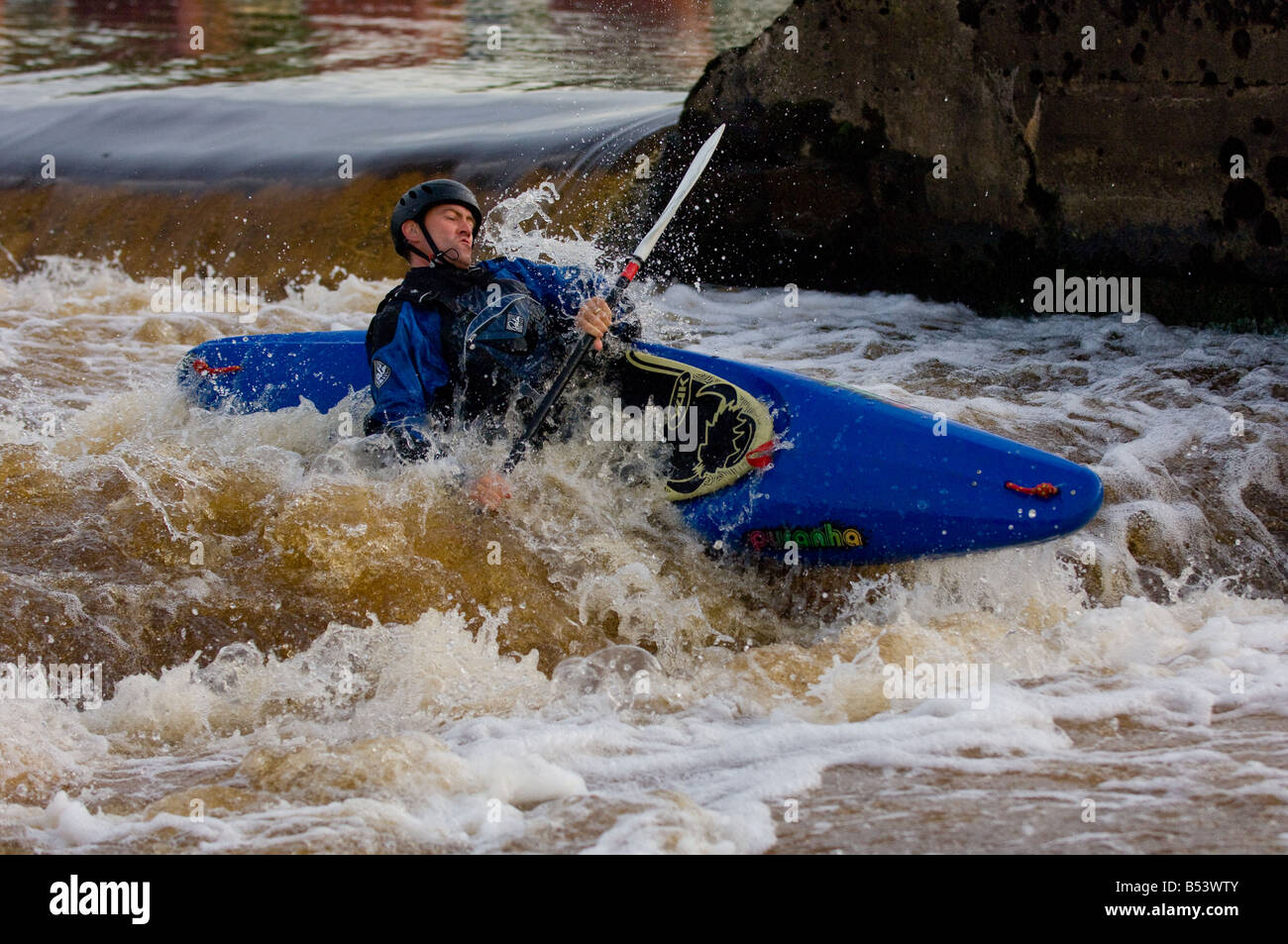 Caucasian male kayaker in a blue kayak capsizing in white water. Stock Photo