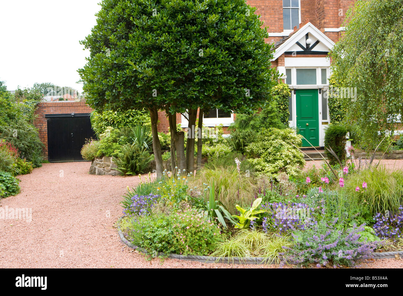 front garden of a large detached house with red gravel driveway and holly bushes Stock Photo