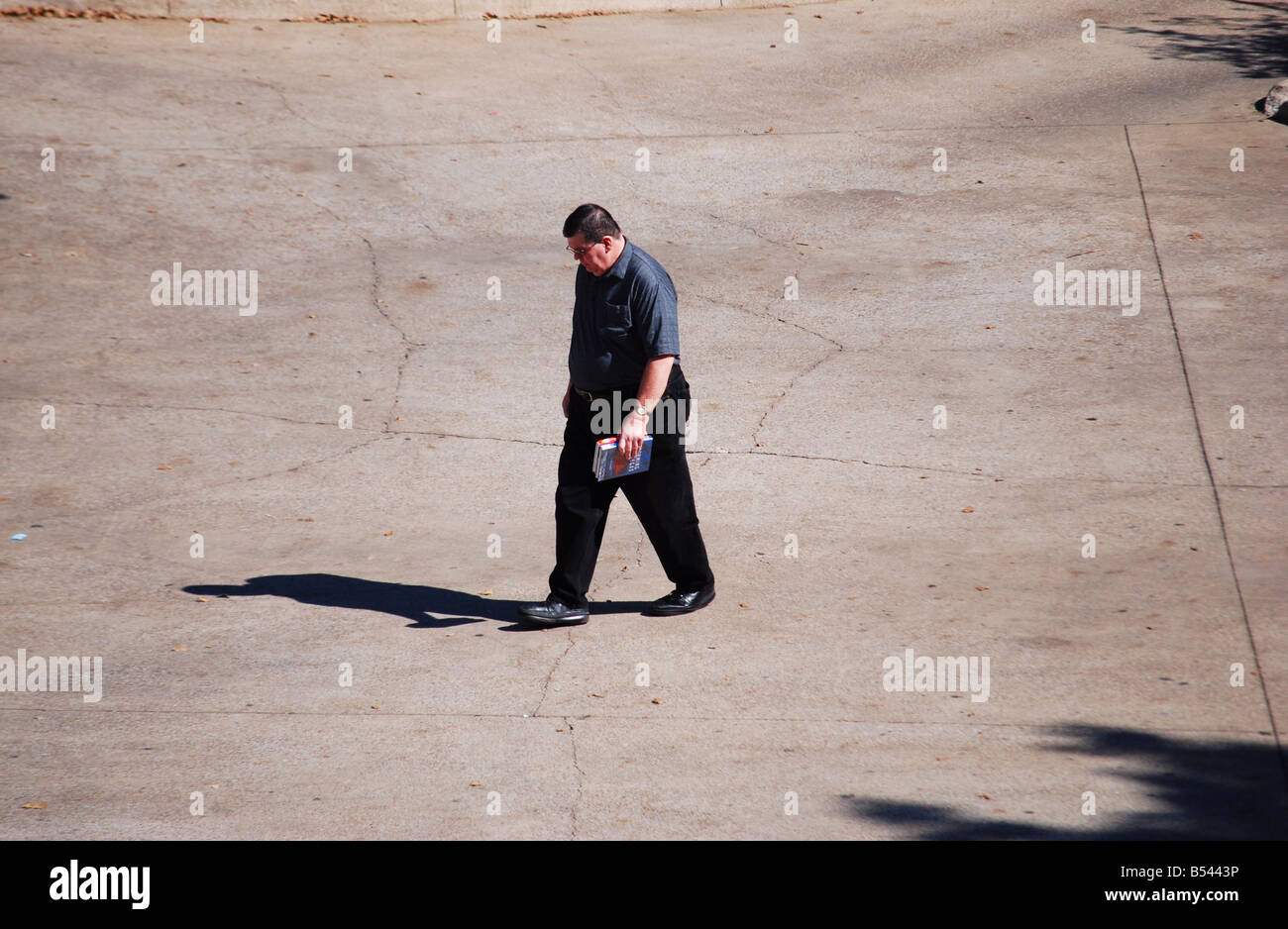 image of a man walking across a library parking lot holding a book Stock Photo