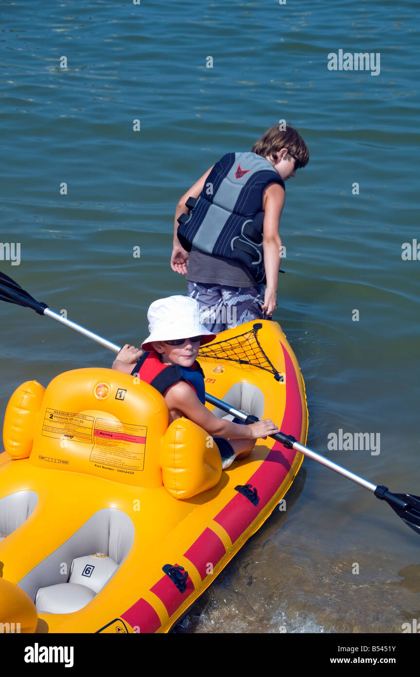 two boys launch inflatable PVC yellow kayak summer watersports Stock Photo