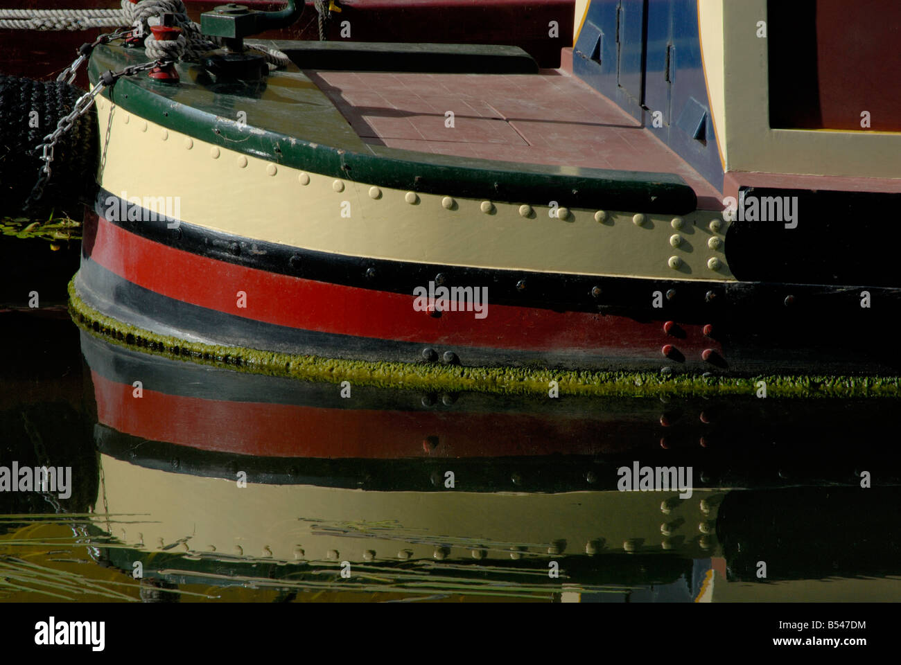 Rivetted stern and tiller of a traditional narrowboat reflected in the Slough Arm of the Grand Union Canal, Iver, London Stock Photo