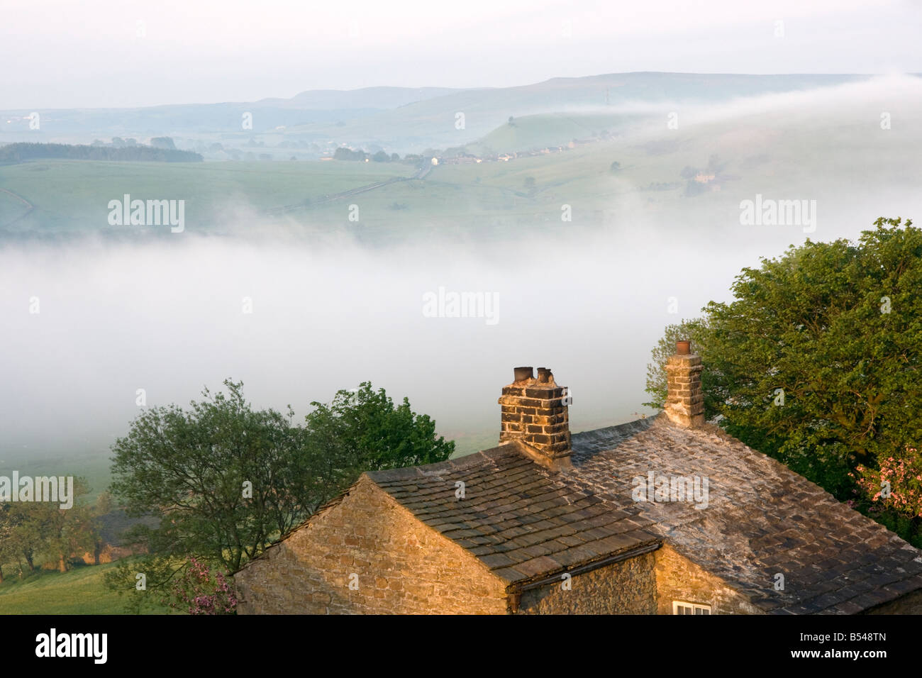 traditional stone built english farmhouse at rushup edge in the peak district by morning light with mist in the landscape Stock Photo