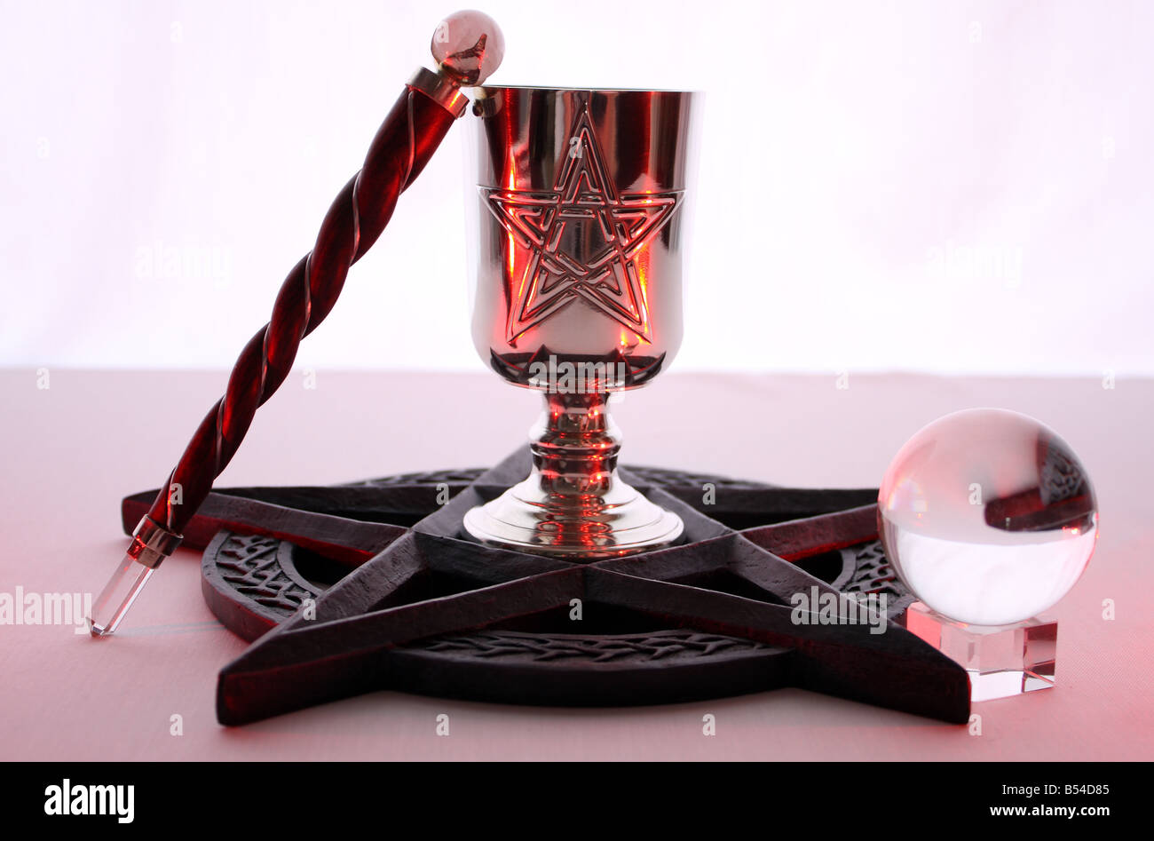 An altar ritual set up on a white background, using a Pentacle, Gemstone Quartz Chalice, Wand and Crystal Ball. Stock Photo