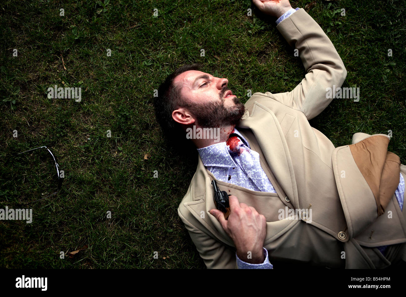 A man lies with a hand gun and blood down his face Stock Photo