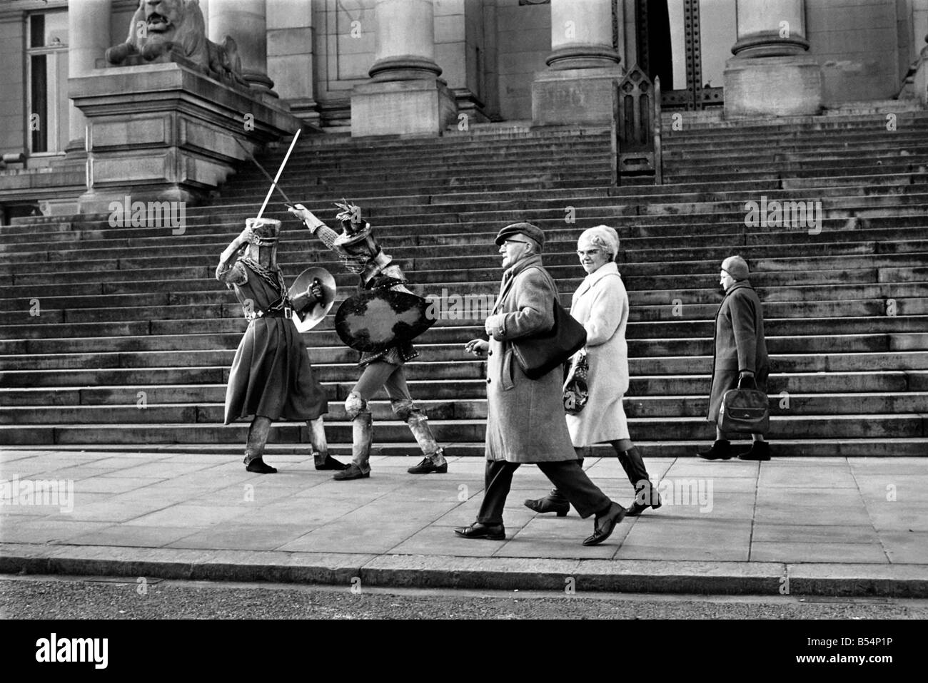 Shoppers hurry past the Town Hall steps as a couple of medieval knights are locked in combat in Bolton. The battle was being filmed by the Bolton Octagan Theatre Company. December 1969 Z11749-001 Stock Photo