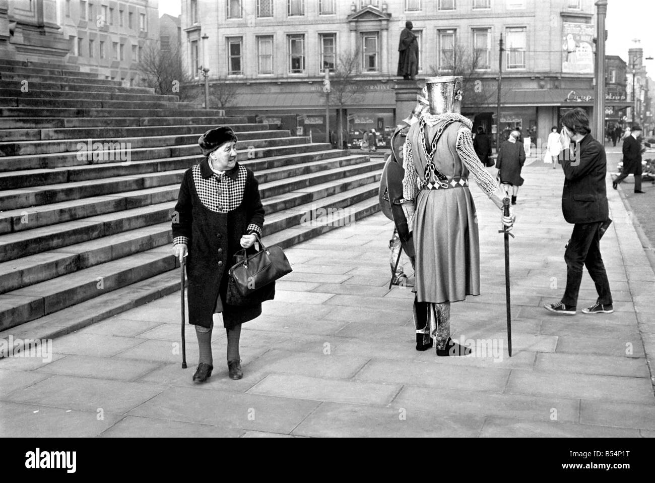 Shoppers hurry past the Town Hall steps as a couple of medieval knights are locked in combat in Bolton. The battle was being filmed by the Bolton Octagan Theatre Company. December 1969 Z11749-002 Stock Photo