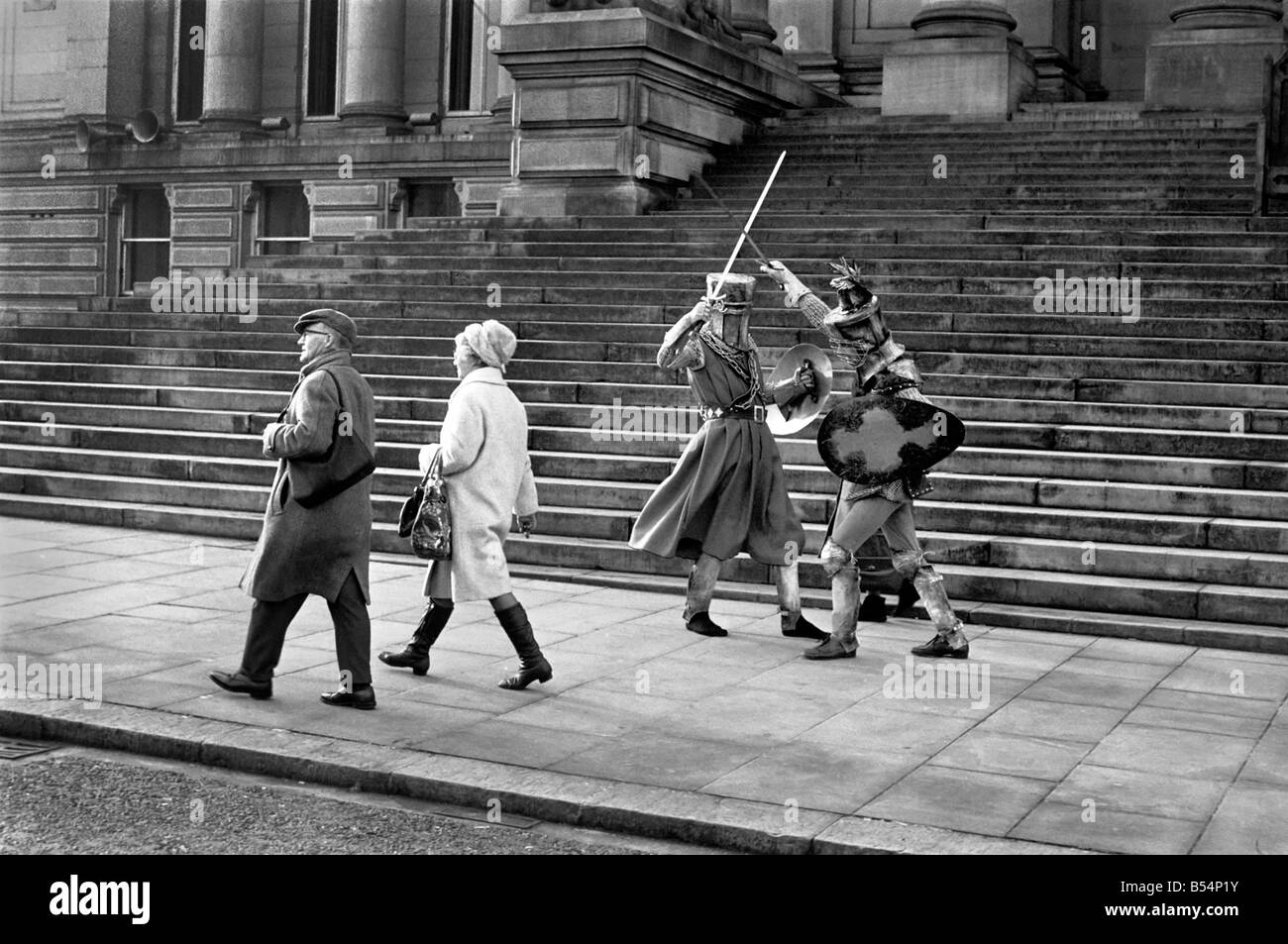 Shoppers hurry past the Town Hall steps as a couple of medieval knights are locked in combat in Bolton. The battle was being filmed by the Bolton Octagan Theatre Company. December 1969 Z11749 Stock Photo