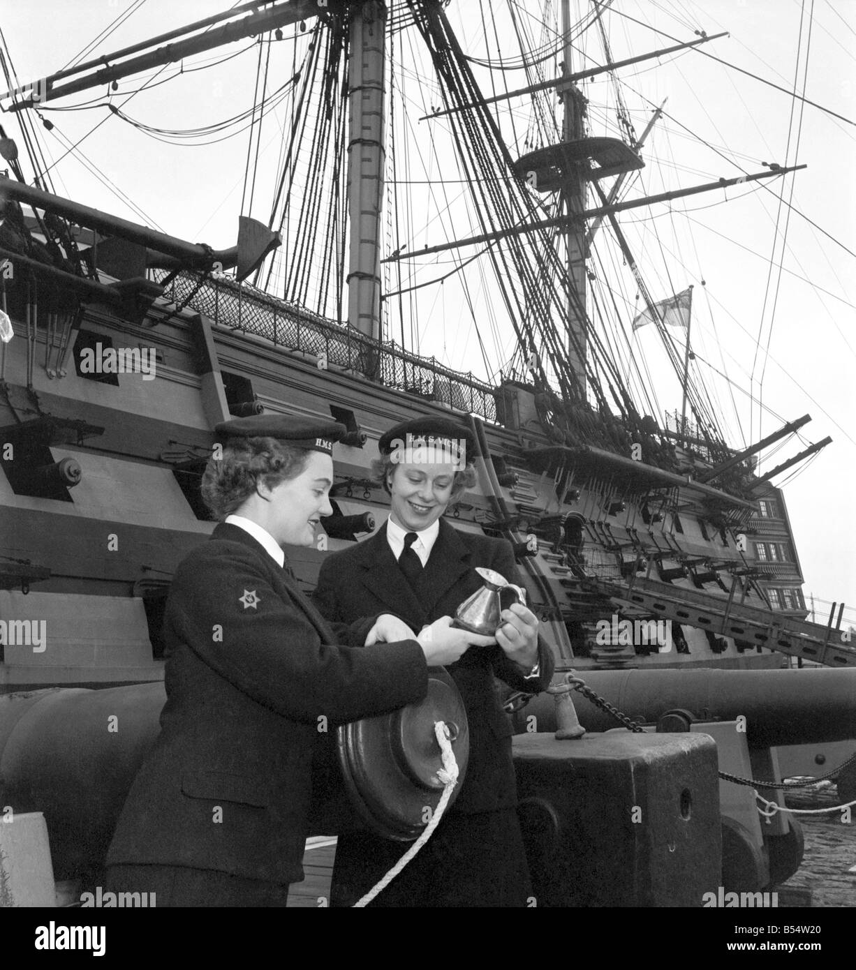 Royal Navy HMS Victory: WREN Margaret Mann 19 a winter in the navy, and Wren Joan Wallen age 20 of Radar Dept. They are intersted in a rum measure used aboard. The victory in Nelson days. October 1953 D615-001 Stock Photo