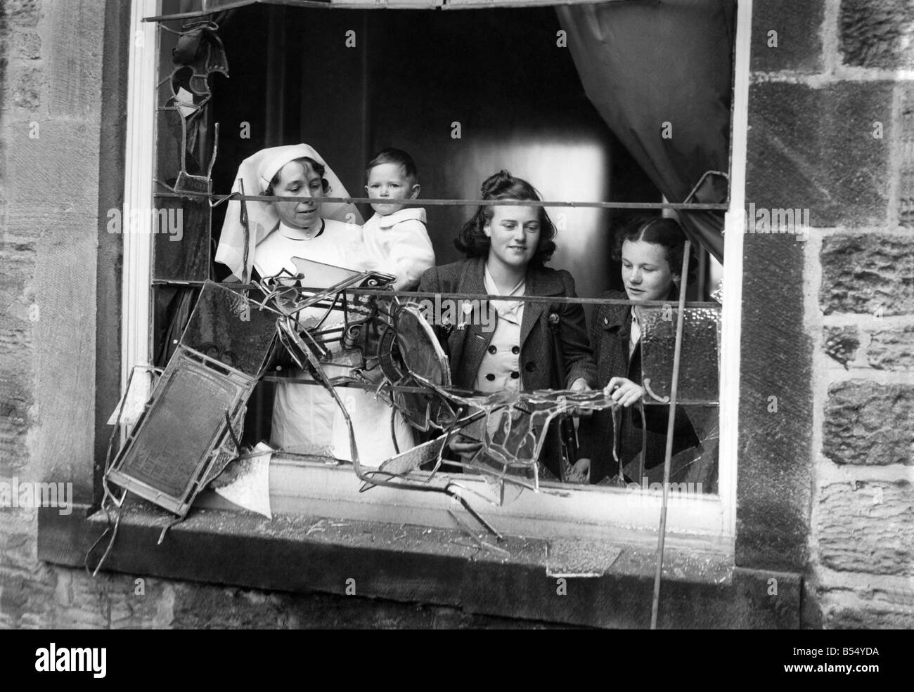 Girls and a nurse holding a litte baby looking out through the smashed window of a bomb damaged maternity unit in a London hospital. ;August 1940 ;P012277 Stock Photo