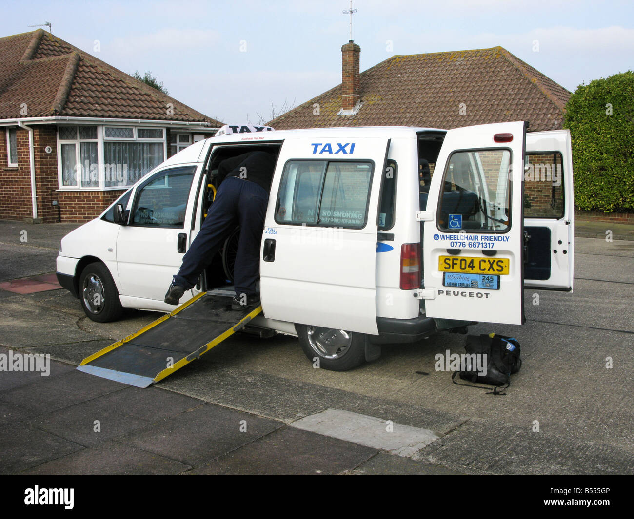 taxi driver putting a slip resistant ramp in place from a wheelchair friendly taxi for the disabled, enabling mobility Stock Photo