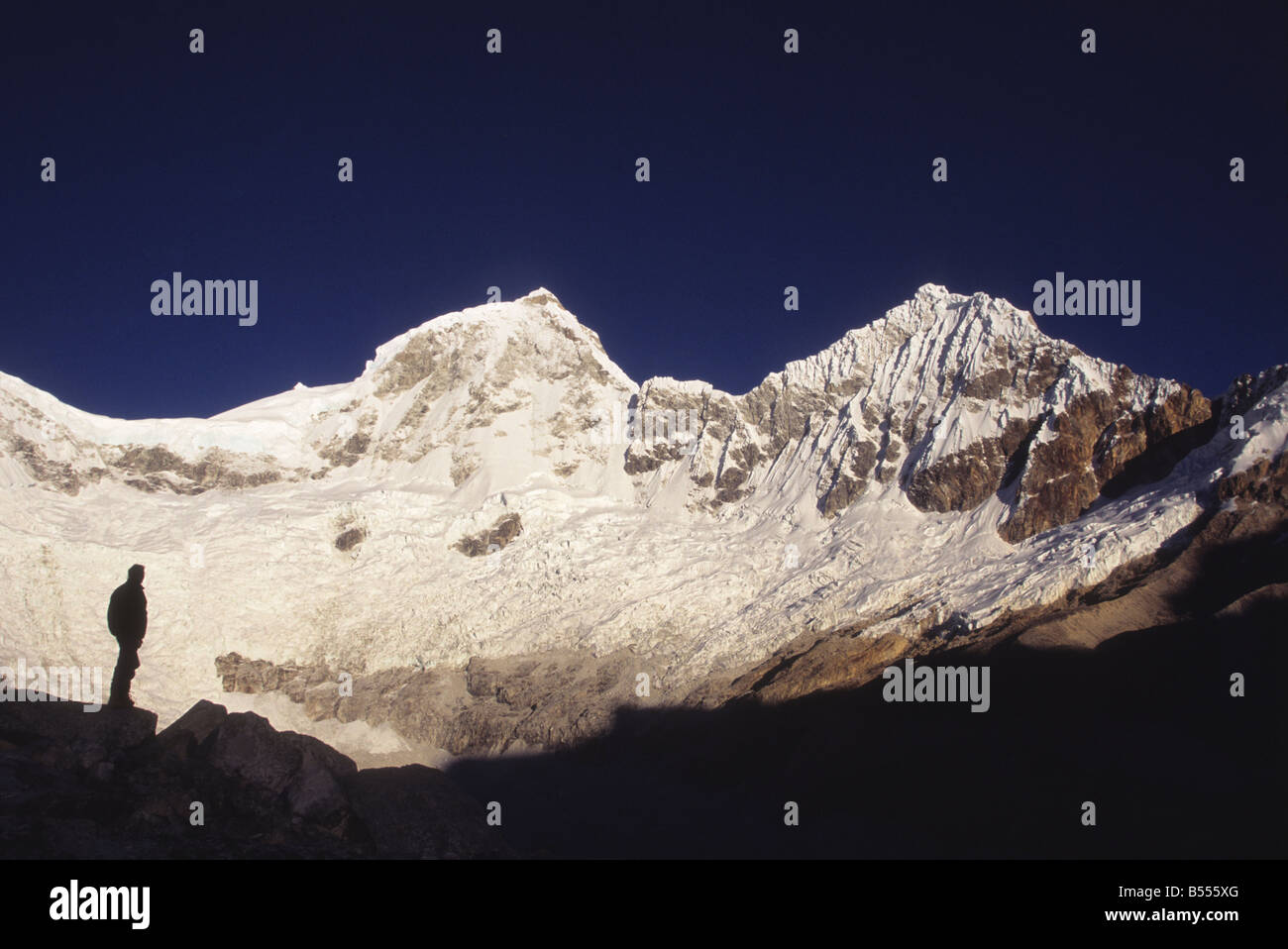 Trekker silhouetted below Mt Huandoy (L to R: East and North Peaks) looking at view, Cordillera Blanca, Peru Stock Photo