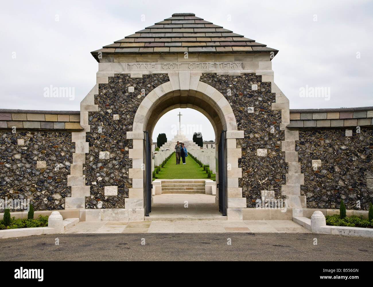 Two people walking between graves at the entrance to Tyne Cot British War Memorial cemetery Belgium Stock Photo