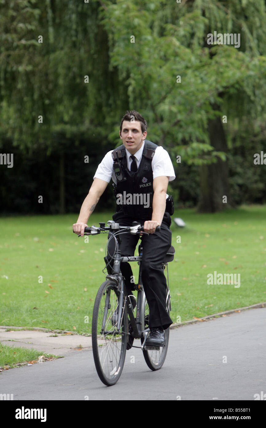 Police man rides bike through park Stock Photo