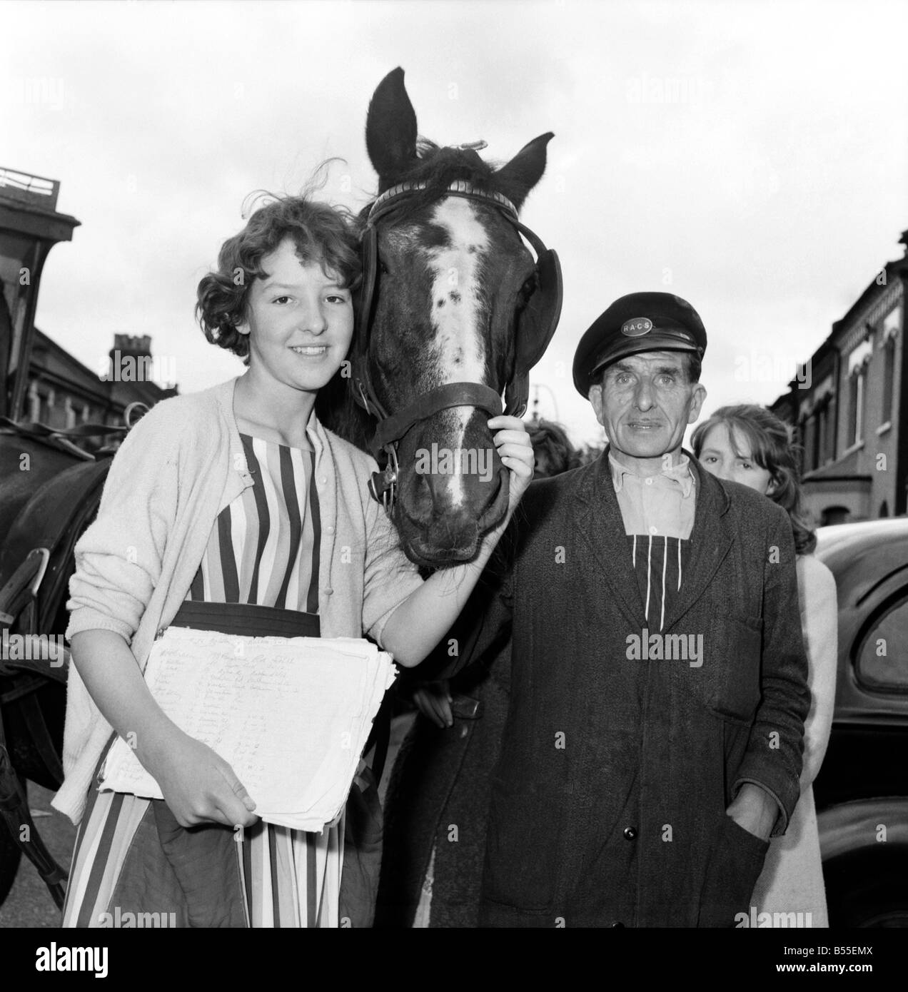 Children petition to save milkmans house: Jennifer here collects a signature in a street market at Bedford Hill, Balham. Signing the book is Mrs. Robert Kelly who has given him a carrot every morning for years. Jennifer gives Eva a carrot on the right is Diane Cathercole who has helped gather signatures. ;June 1960 ;M4407-001 Stock Photo