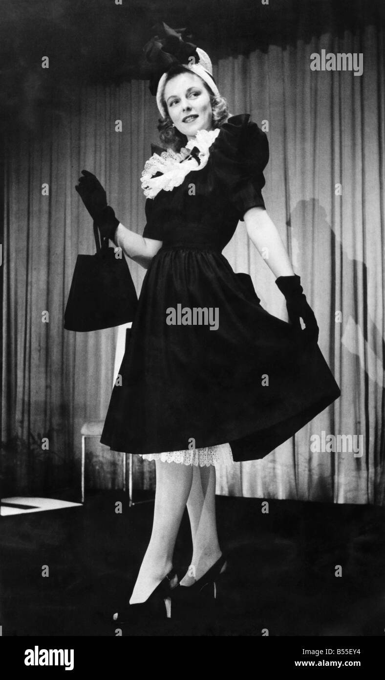 Shown at London's first post-war non-austerity fashion show, a black taffeta frock with a huge bustle at the back, just right for cocktails or a party. The double frill of stiff white lace round the neckline is repeated again on the slip underneath to peep out as the skirt swings while walking. It is topped by a hat made of the same lace and black ribbon. ;May 1946 ;P008732 Stock Photo