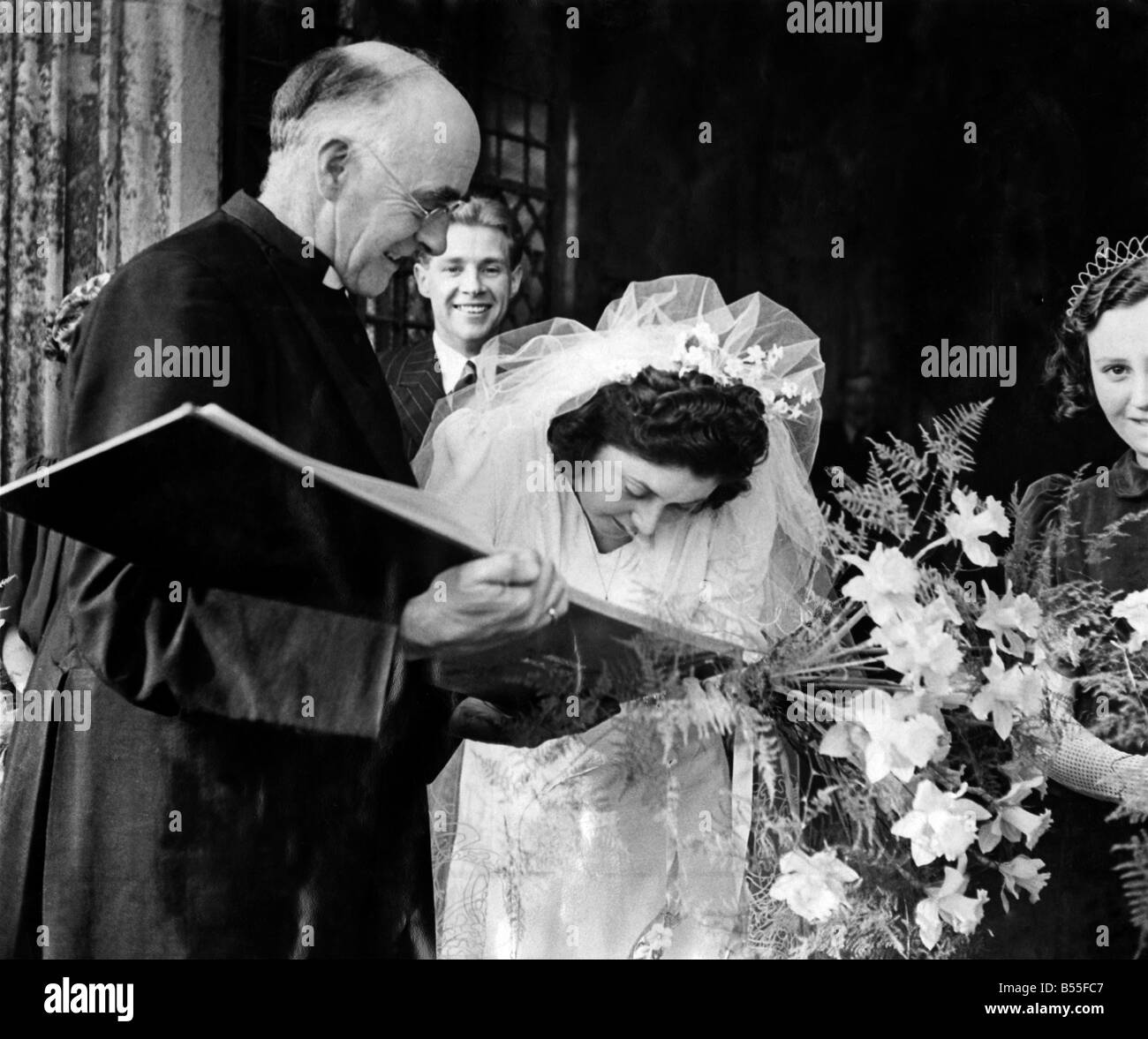 This bride forgot to sign the register. The Rector, Canon Whytehead hurried after the newlyweds and smiles as he holds the register for Mrs. Deal to sign outside St. Margaret's Church, Lowestoft yesterday. ;March 1943 ;P011592 Stock Photo