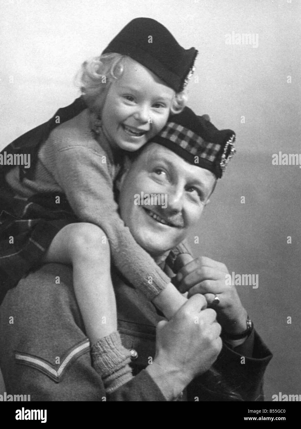 Young girl wearing a hat with tartan design sitting of her father's shoulder, wearing military uniform;Circa 1945;P044445 Stock Photo
