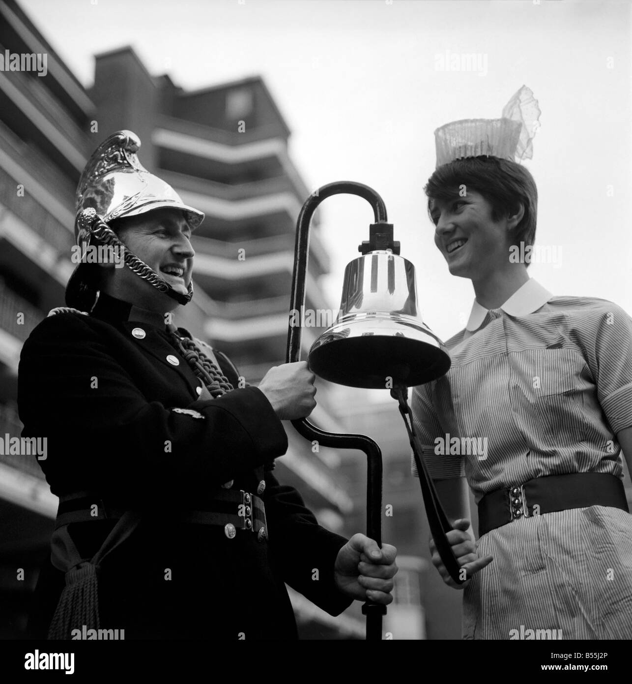 21 year old nurse, Angela Wyatt from St. Thomas's hospital went to the London fire Brigade Headquarters, Lambeth, to collect a fire bell which was wanted on loan for The Malcolm Sargent Cancer fund for children, Christmas Carol concert held at the festival hall. Trying out the fire bell with Leading Fireman Joe Wills, is Nurse Angela Wyatt. December 1969 Z12149 Stock Photo