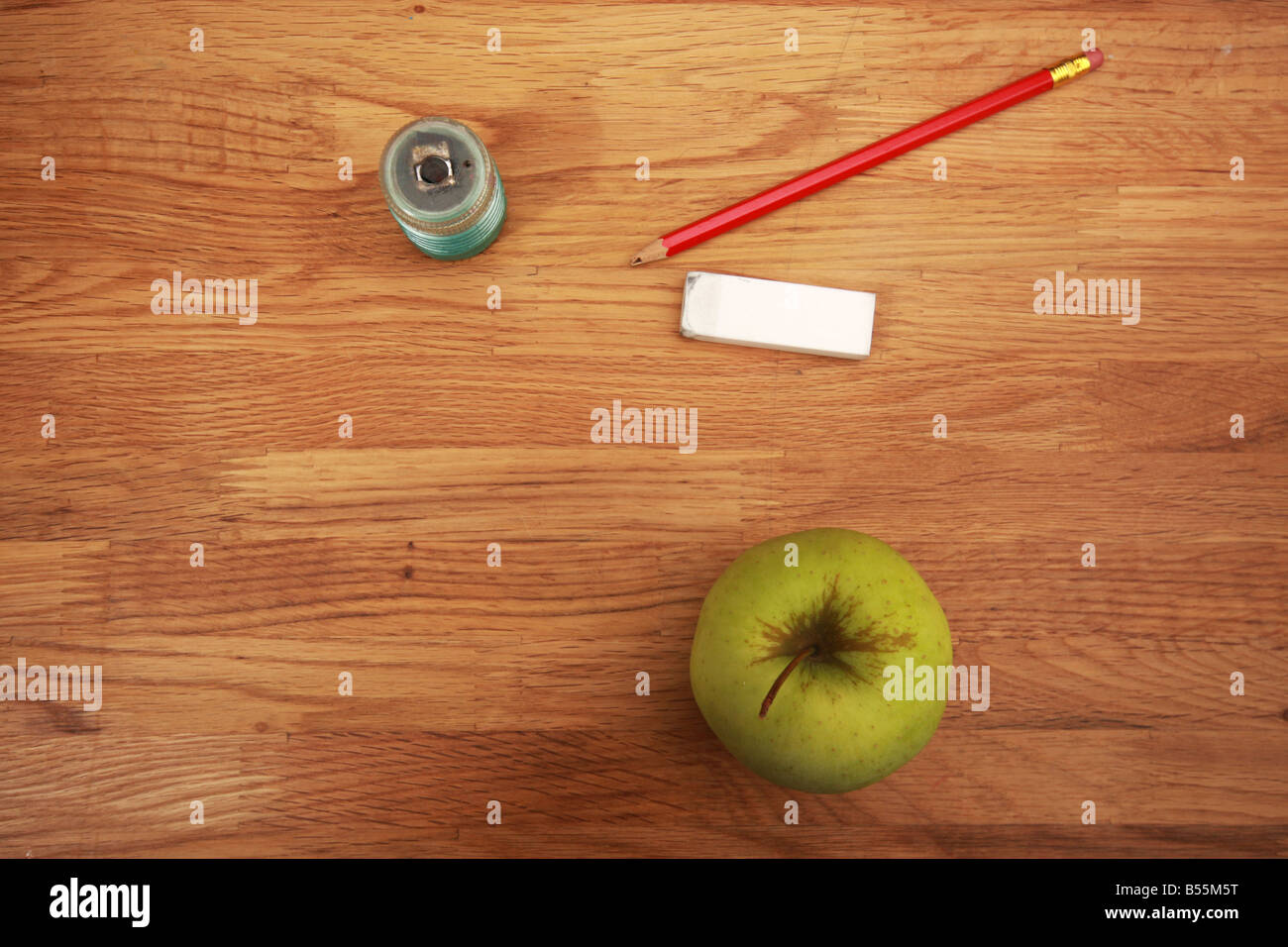 pencil eraser sharpener and apple lying on a school table Stock Photo