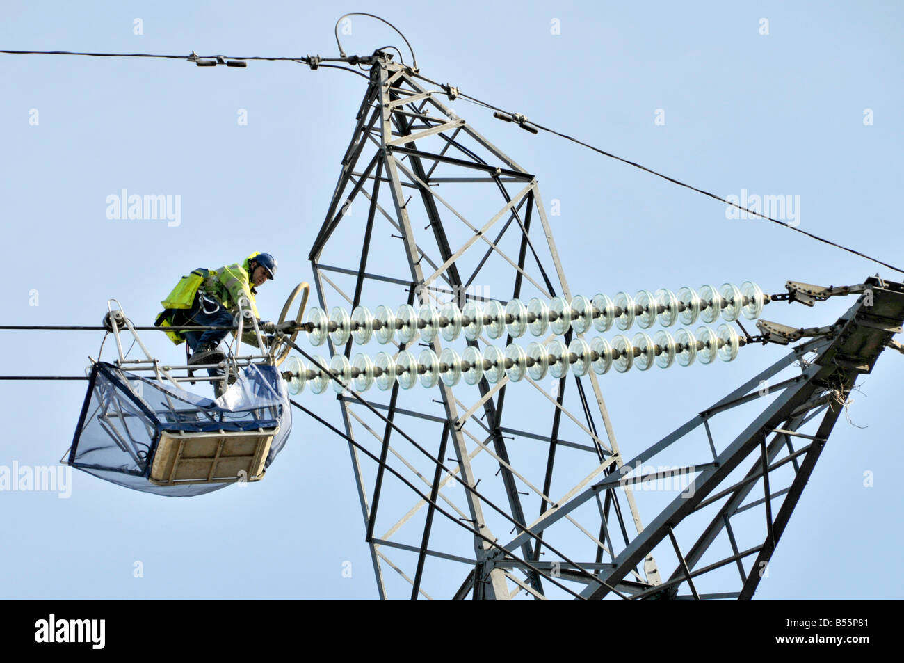 One of a team of electrical engineers working from trolley cradle on high voltage power lines & pylons above Stratford East London England UK Stock Photo