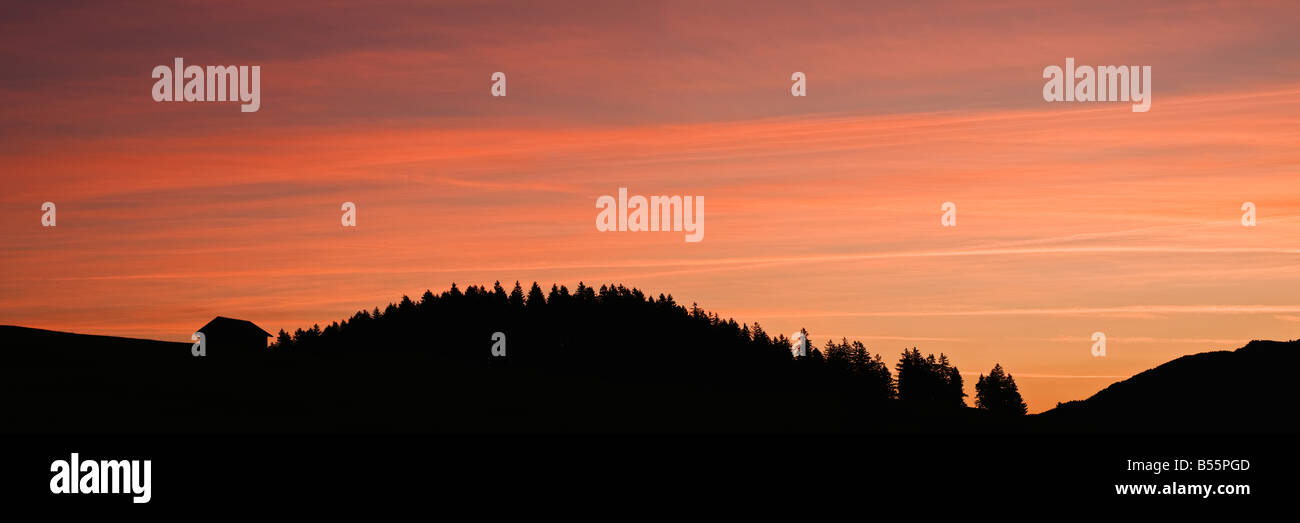 Silhouette of Barn and forest against colorful sky at sunrise Allgäu Bavaria Germany Stock Photo