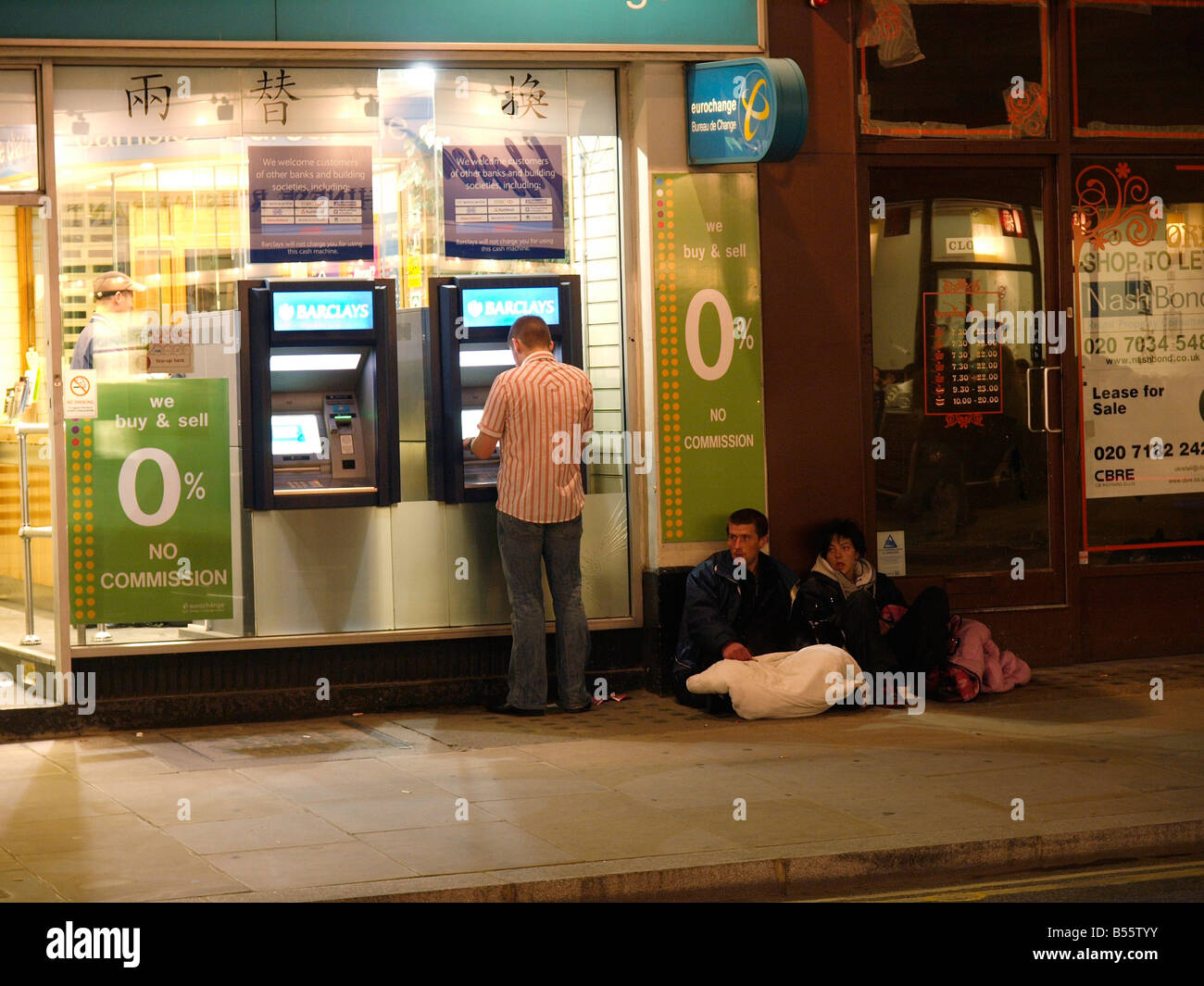 Financial crisis, hard times for some in 2008. Man getting cash from a Barclays ATM with beggars sitting next to it London UK Stock Photo