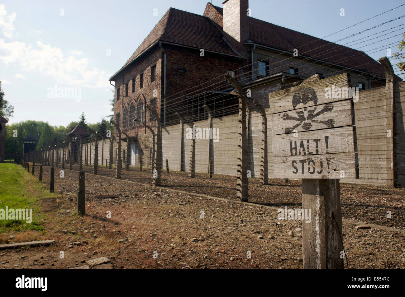 Warning stop sign with skull&bones symbol in front of barbed wire electrified fence in former concentration camp Auschwitz I Stock Photo