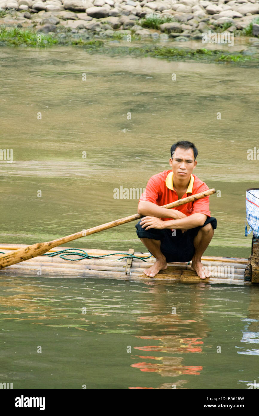 A Chinese man sitting on a bamboo raft holding an oar, Li River, China ...