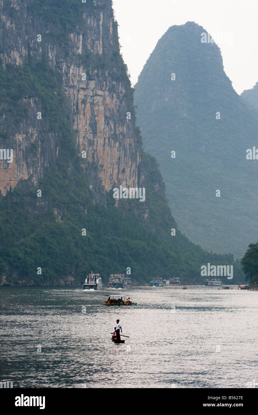 A bamboo raft and tourist boats float down the Li River, China with hills and mountains in the background Stock Photo