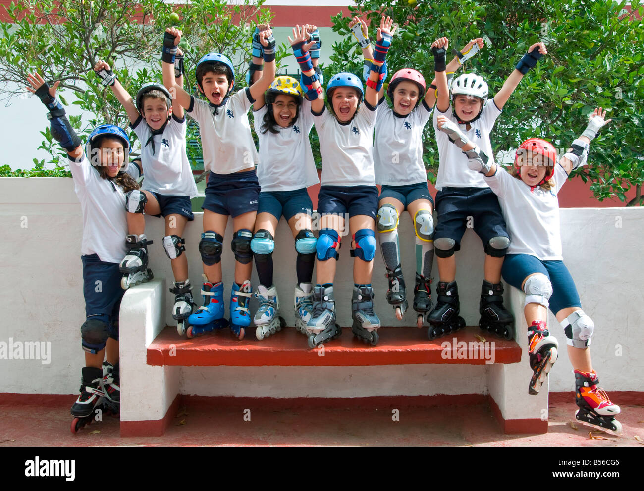 School Photo roller blade team group of happy junior school children wearing safety helmets and knee pads wave together in school playground Stock Photo