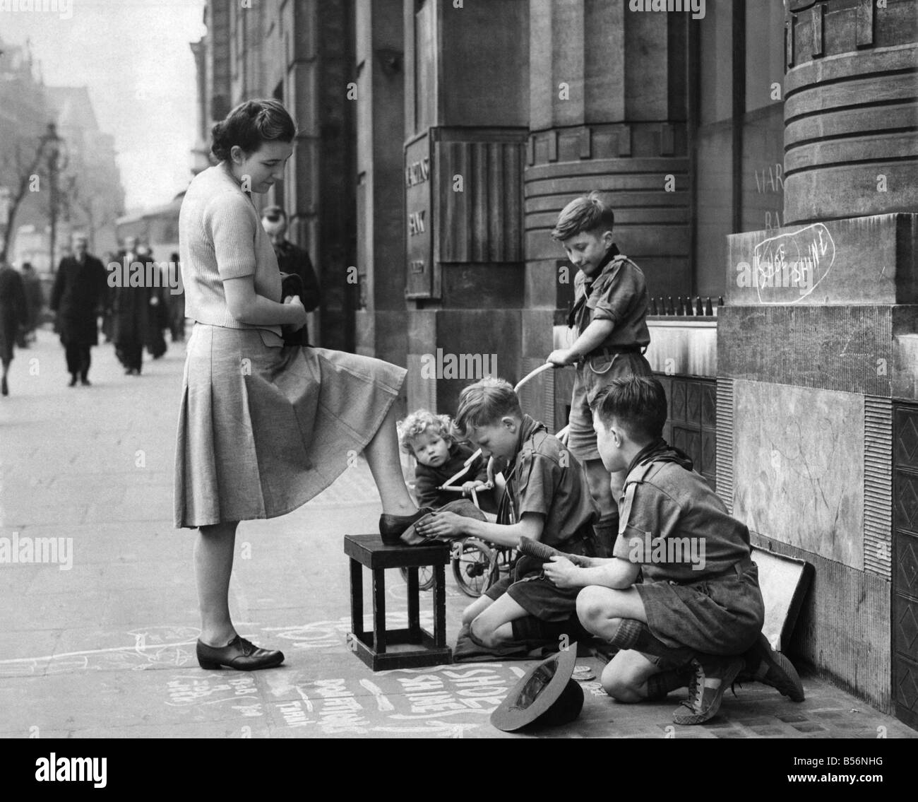 Bob a Job. Three scouts, Left to right, Dennis Hunter, aged 12, Ronald Dury, aged 12, polishing shoes and his twin brother Raymond, with brush in hand took up a profitable site in Kingways to help their cause. This morning, starting at 9.30 am. until 12.30 p.m., the three scouts took £1, 12s. 3d. for their morning's work and 19/6d. during the first two hours of their afternoon duty. The Dury twins, to add colour to their cause brought their youngest brother, Eric, aged 2 along with them for the day. P009995 Stock Photo