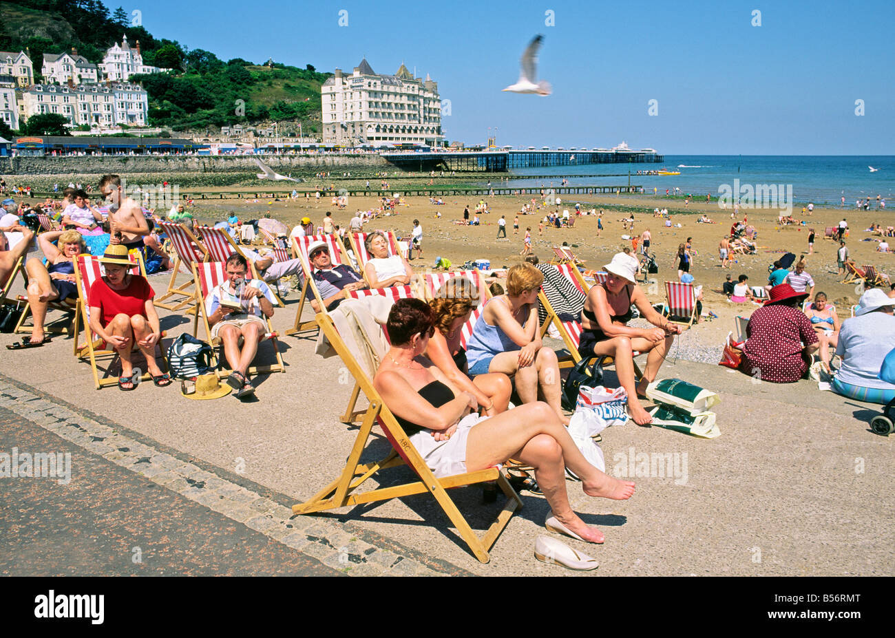 Llandudno seaside resort, Gwynedd, north Wales, UK. Summer holidaymakers sit on deckchairs on the beach seafront Stock Photo