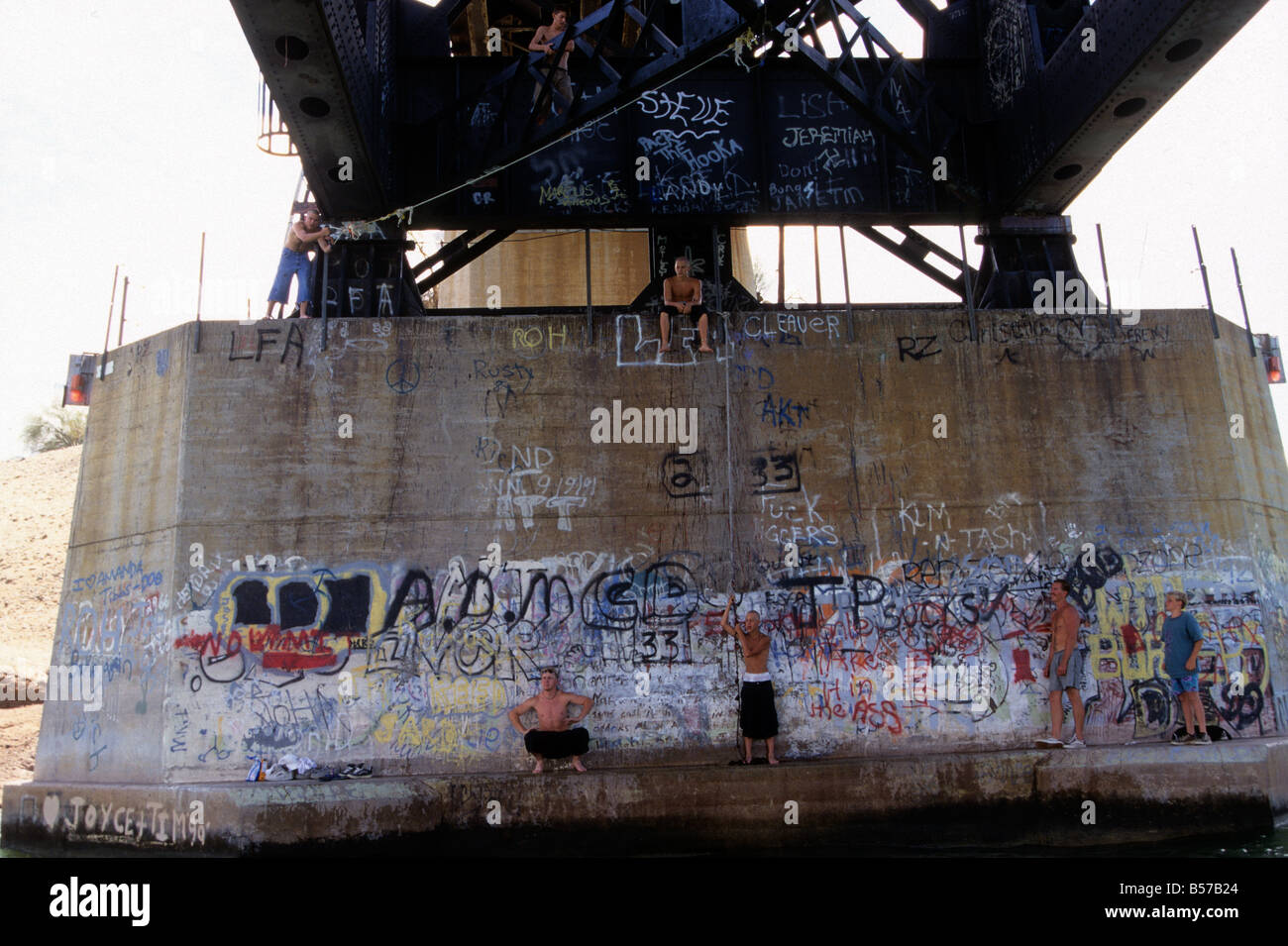 Teenage boys swing from ropes under a bridge over the Colorado River