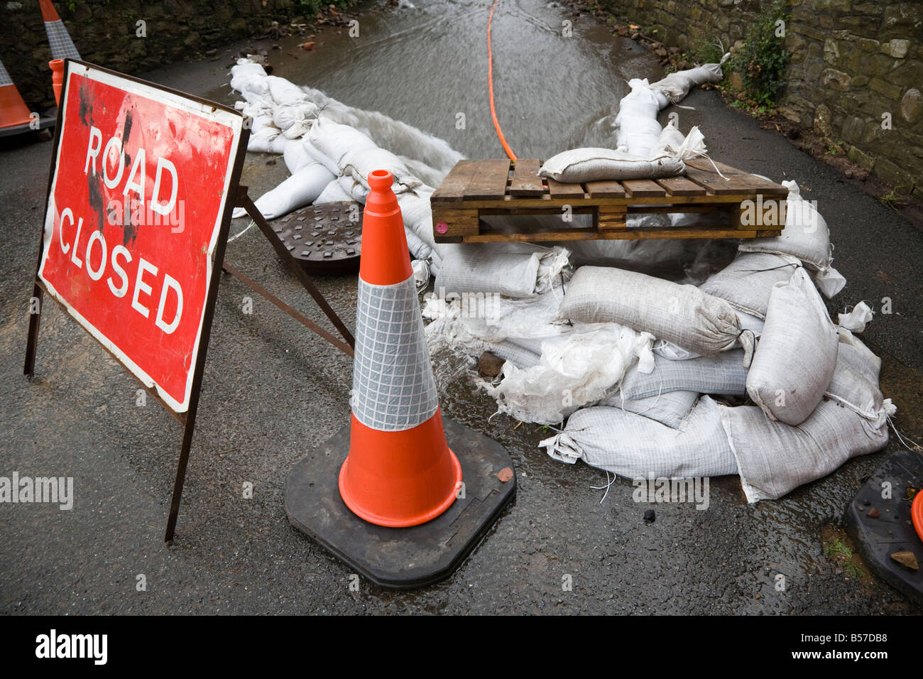 Road closed sign due to flooding with sandbags directing water into manhole Wales UK Stock Photo