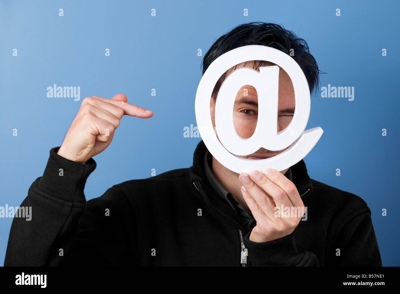 A man who points to the at symbol, seeming indicating 'Please, send me an e-mail'. Homme en train de montrer le symbole arobase. Stock Photo