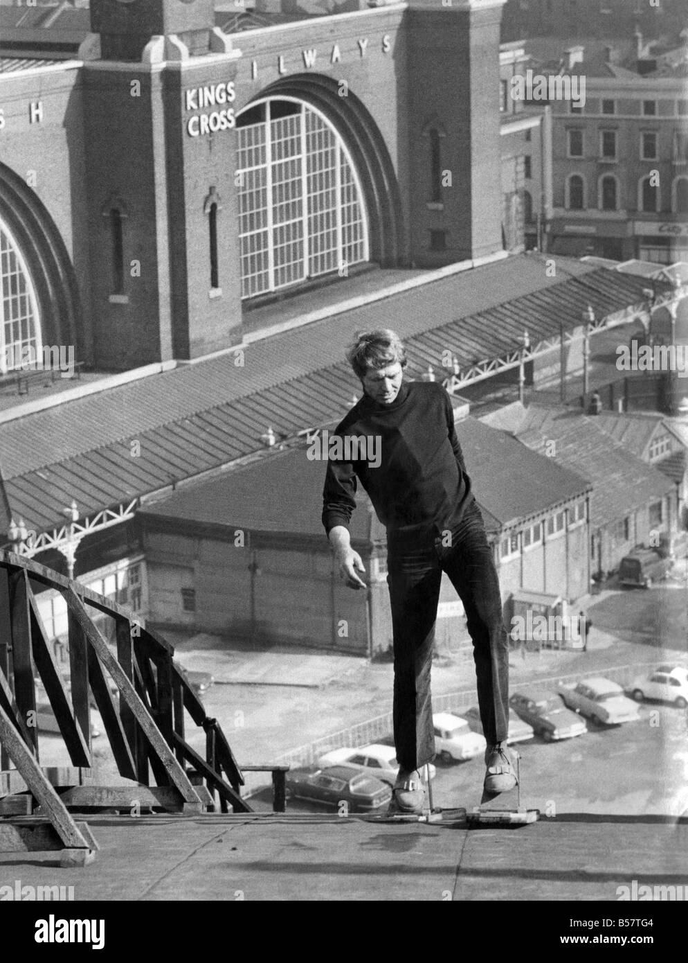 William Willard a 'Tomorrows World' reporter using the Roof Shoes on the slopes of St Pancras Station roof. The shoes were invented by a Welshman to get over the difficulty of fixing aerials to chimneys and other roof jobs. The shoes are adjustable in three positions which enables the user to walk in an upright position, on a roof of 45 degrees angles. The shoes are made of alaminuim with sponge rubber bottoms, which enables the user to walk up and down even wet roofs. October 1970 P004296 Stock Photo