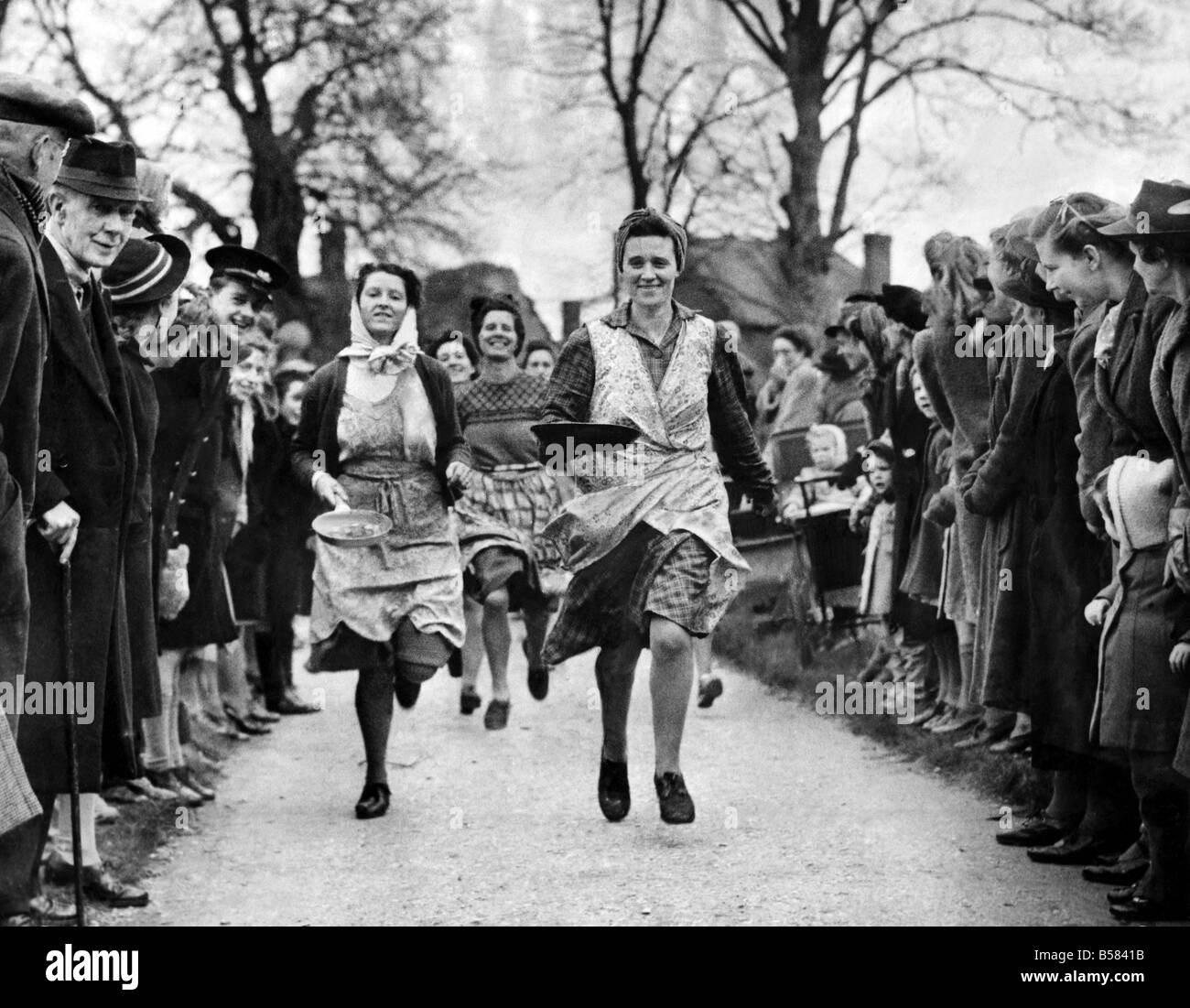 A revival of a five hundred year old custom took place at Olney. Bucks. To-day when housewives took part in the traditional Pancake Day Race. Starting at the Parish Pump in the Town Square the competitors had to run a quarter of a mile to the Parish Church, 'Tossing ' their pancakes en route. The reward for the winner was a kiss from Verger W.K. Mynard, the bellringer, who started the race. All the competitors and many hundreds of townspeople who watched the race were welcomed by the Vicar the Rev. R.C. Collins and afterwards joined in a short service in the Parish Church Stock Photo