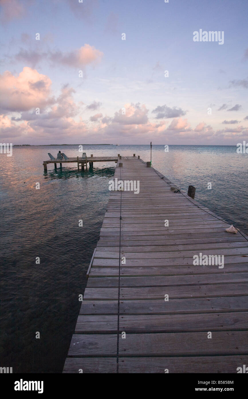 People sitting on chair on jetty at sunrise, Tobaco Caye, Belize, Central America Stock Photo