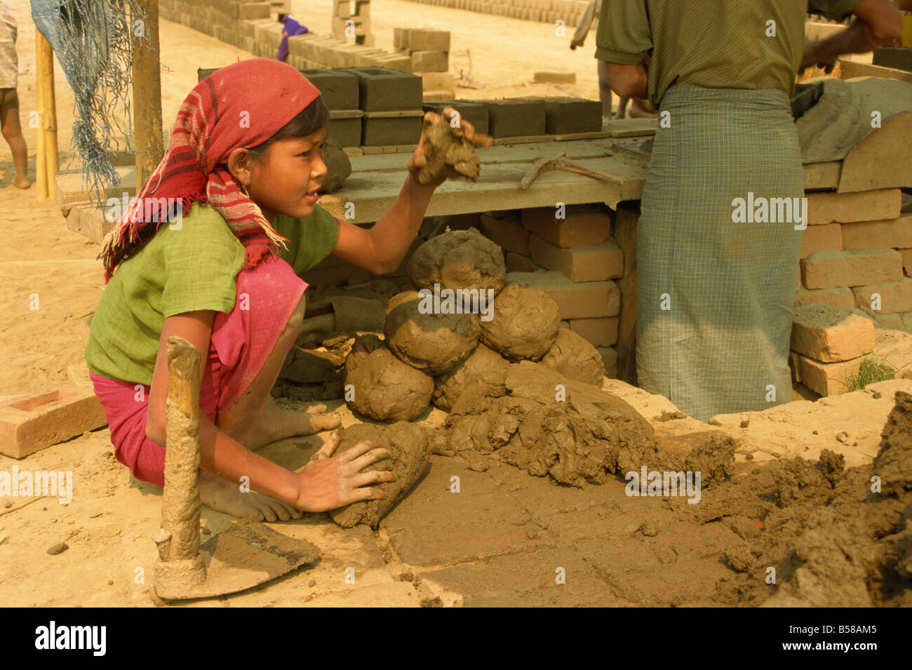 Child labour young girl moulding lumps of clay at brickworks on