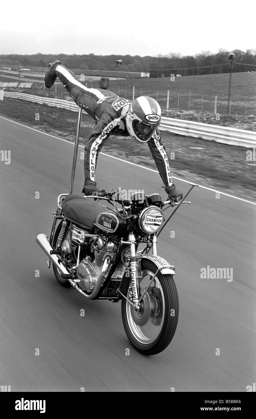 Motorbike stunt: Dave Taylor lives at Barnhurst near Bexley Kent. He is married with three children. Dave is performing a tank stand at 90 M.P.H. along the finishing straight at brands hatch racing circut. This was a slow run. He has done this at over 100 M.P.H. April 1977 77-02121-003 Stock Photo