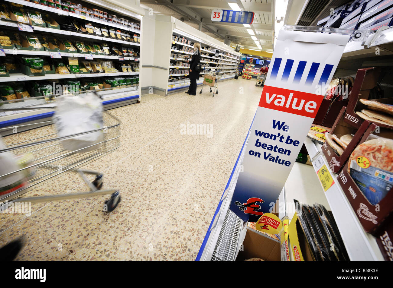 Tesco value: a businessman with shopping trolley walking down a refrigerated aisle of pizza and pasta. Stock Photo