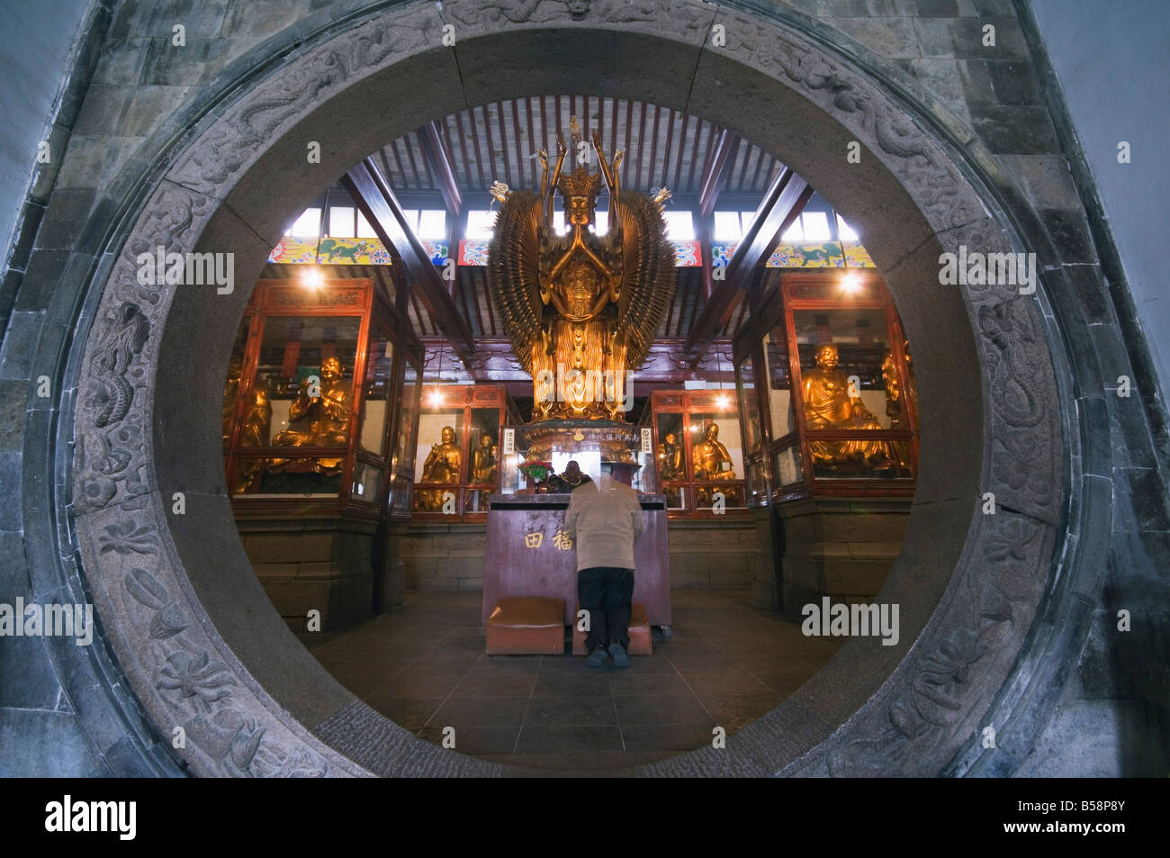 A woman praying in front of an arched entrance at West Garden Buddhist Temple, Suzhou, Jiangsu Province, China Stock Photo