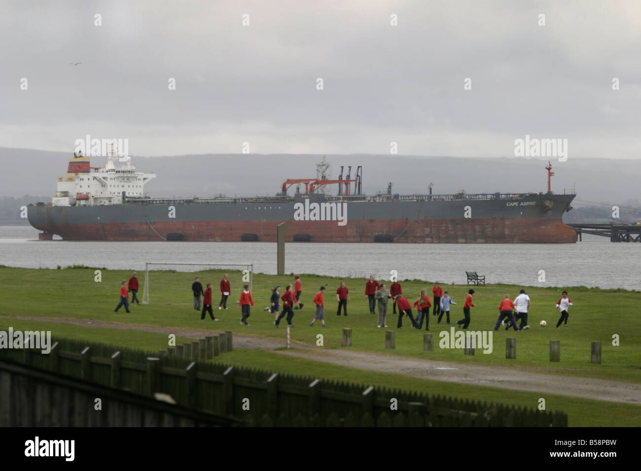 School children play football on the Links Cromarty while oil tanker loads up at Nigg oil terminal Stock Photo