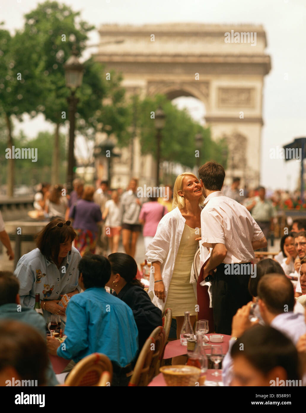 Greeting friends at an outdoor cafe on the Champs Elysees with the Arc de Triomphe behind Paris France Europe Stock Photo
