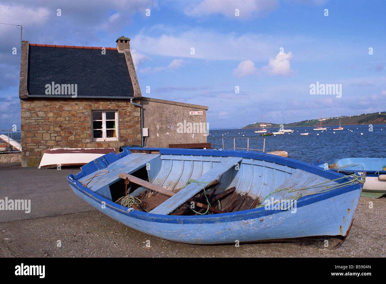Blue boat on shore with the harbour of Le Fret behind Brittany France G Thouvenin Stock Photo